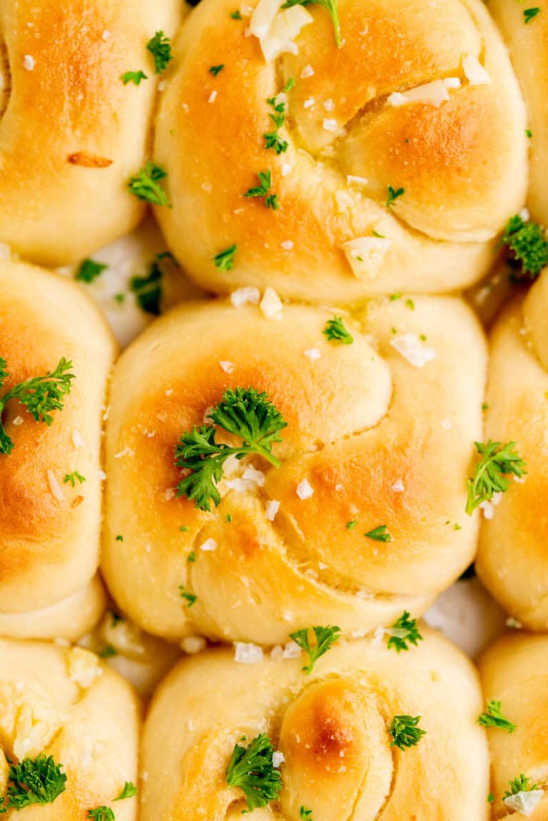 Golden brown sourdough garlic knots topped with chopped parsley and coarse salt, closely arranged together in a baking dish.