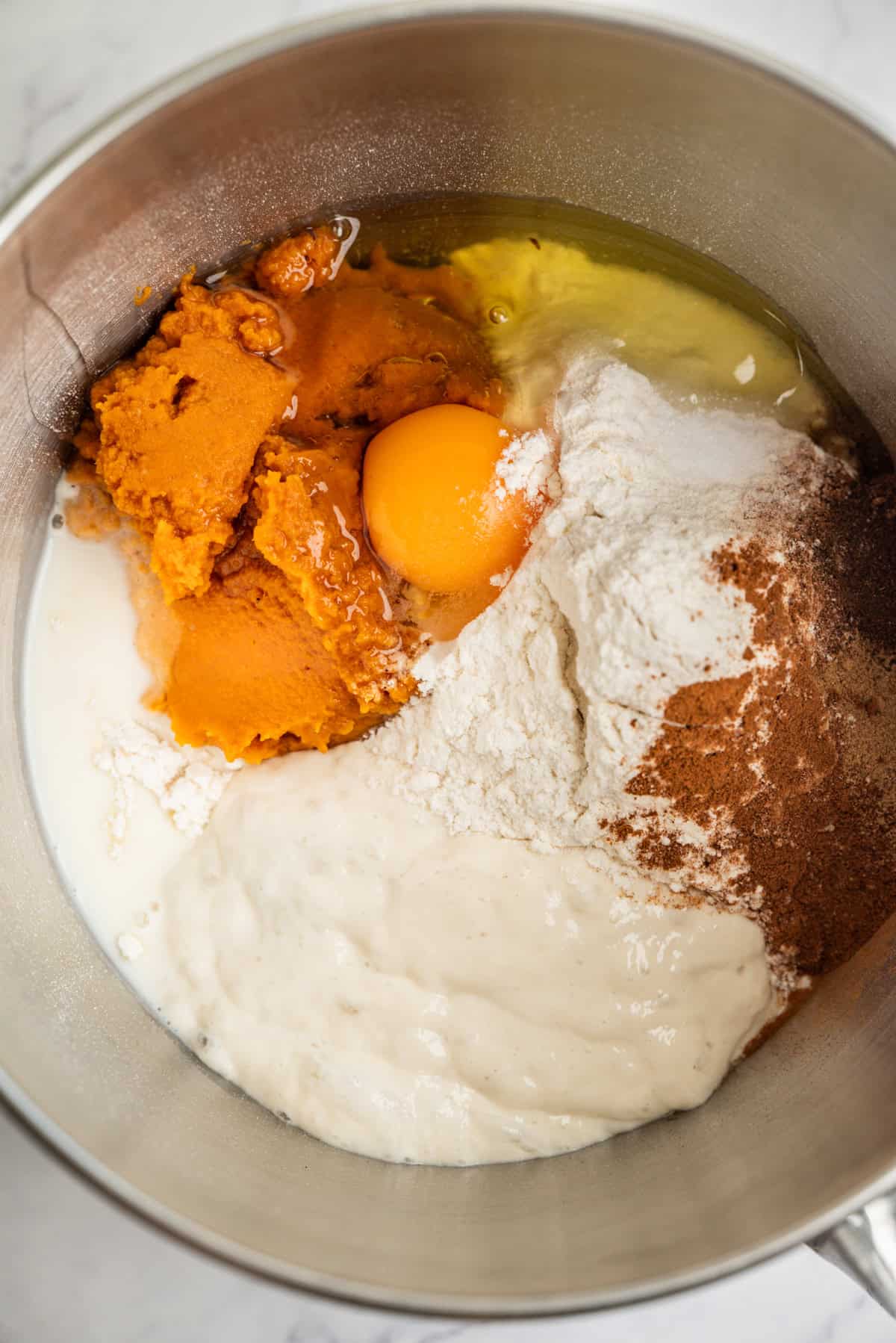 A mixing bowl with pumpkin puree, an egg, flour, milk, sourdough starter, and spices before being mixed together.