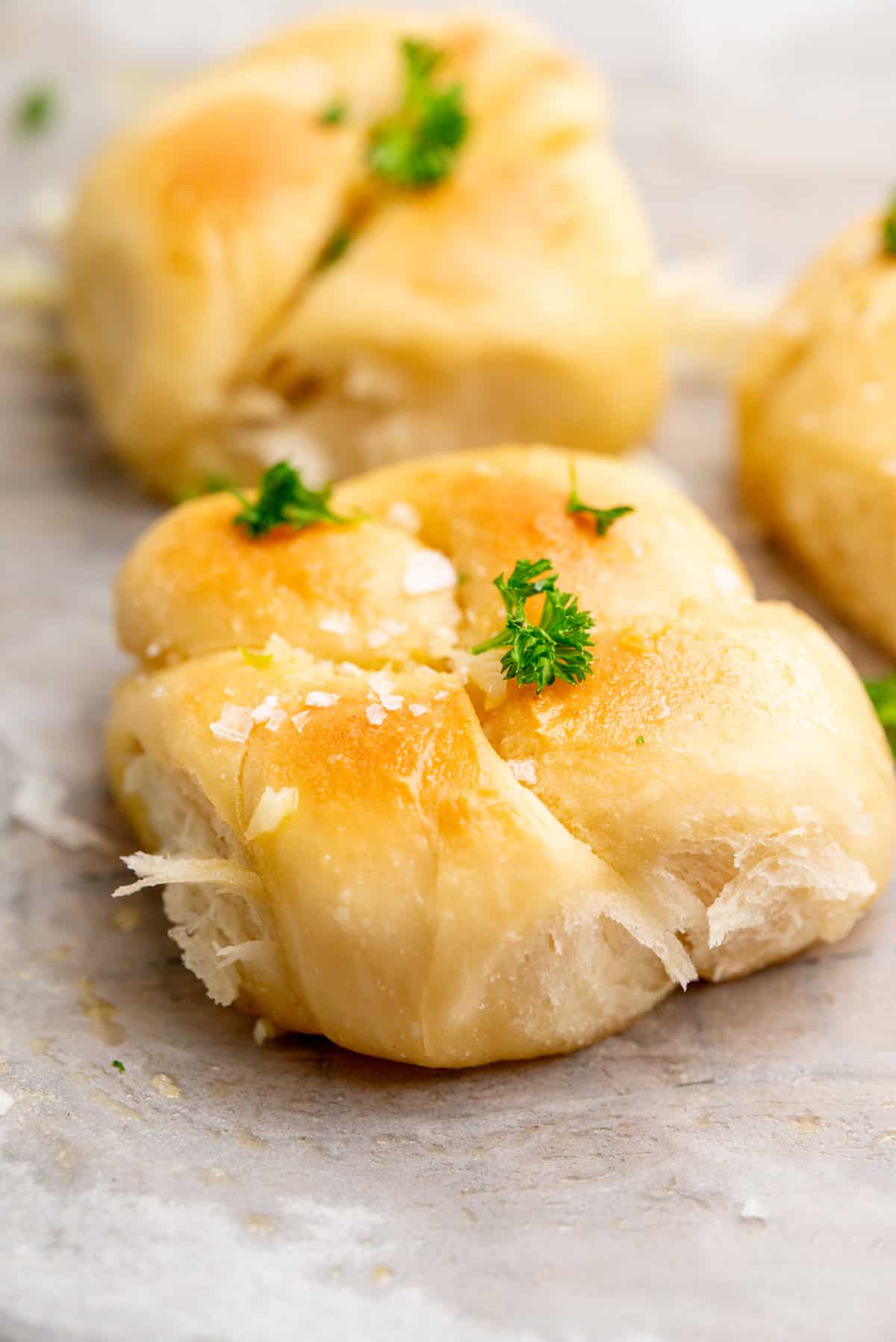 Golden, fluffy garlic knots topped with flaky sea salt and fresh parsley, resting on a sheet of parchment paper.