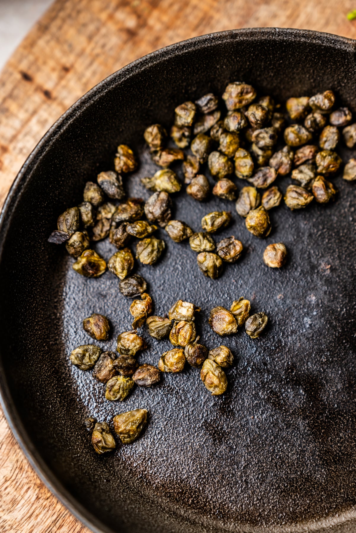A scattering of fried capers in a black cast-iron skillet.