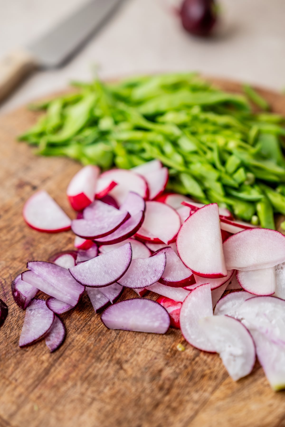 Sliced red radishes and chopped green snap peas on a wooden cutting board.