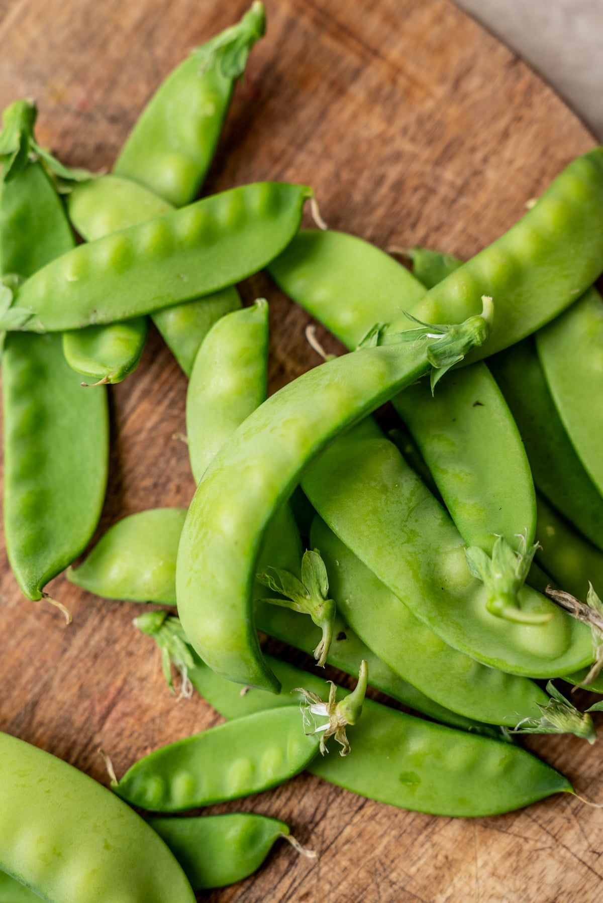 A pile of fresh green snap peas on a wooden cutting board.