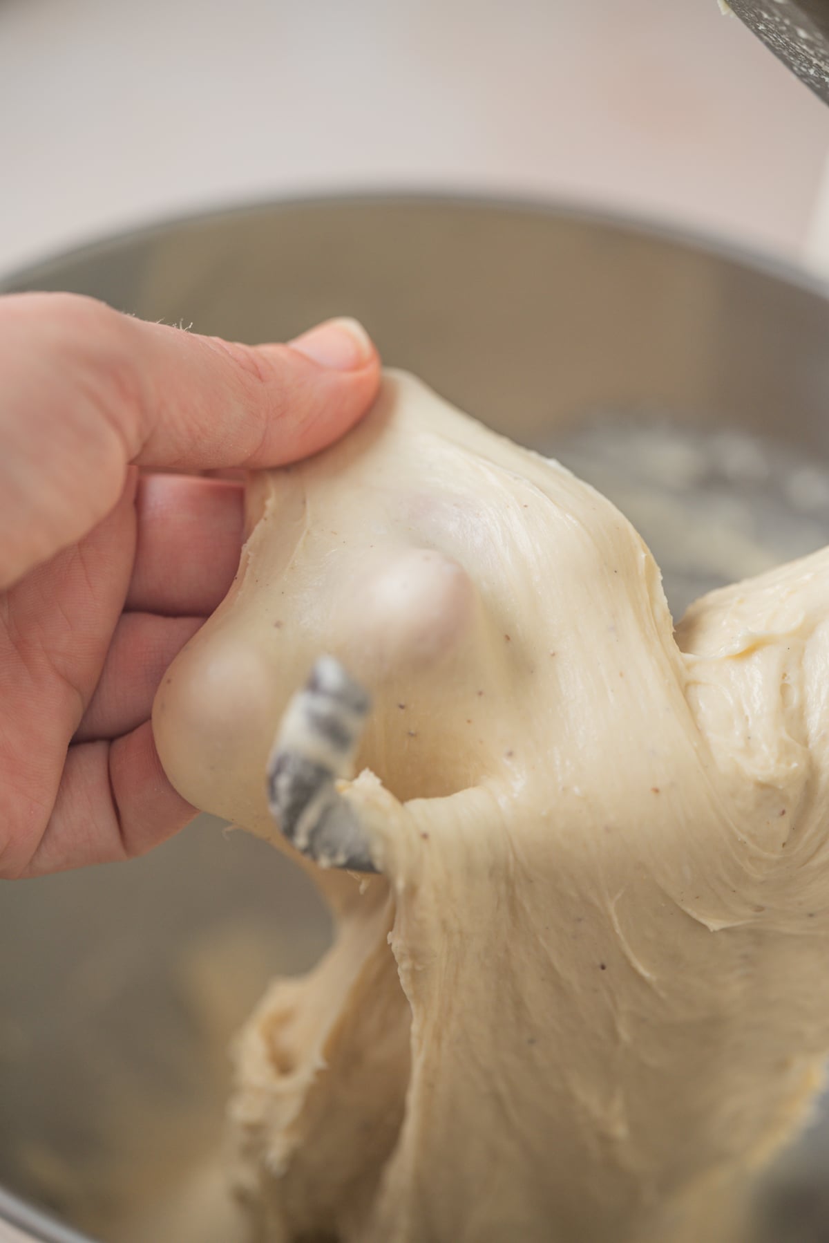 A hand stretches a piece of dough to check for gluten development, showing a translucent windowpane effect.