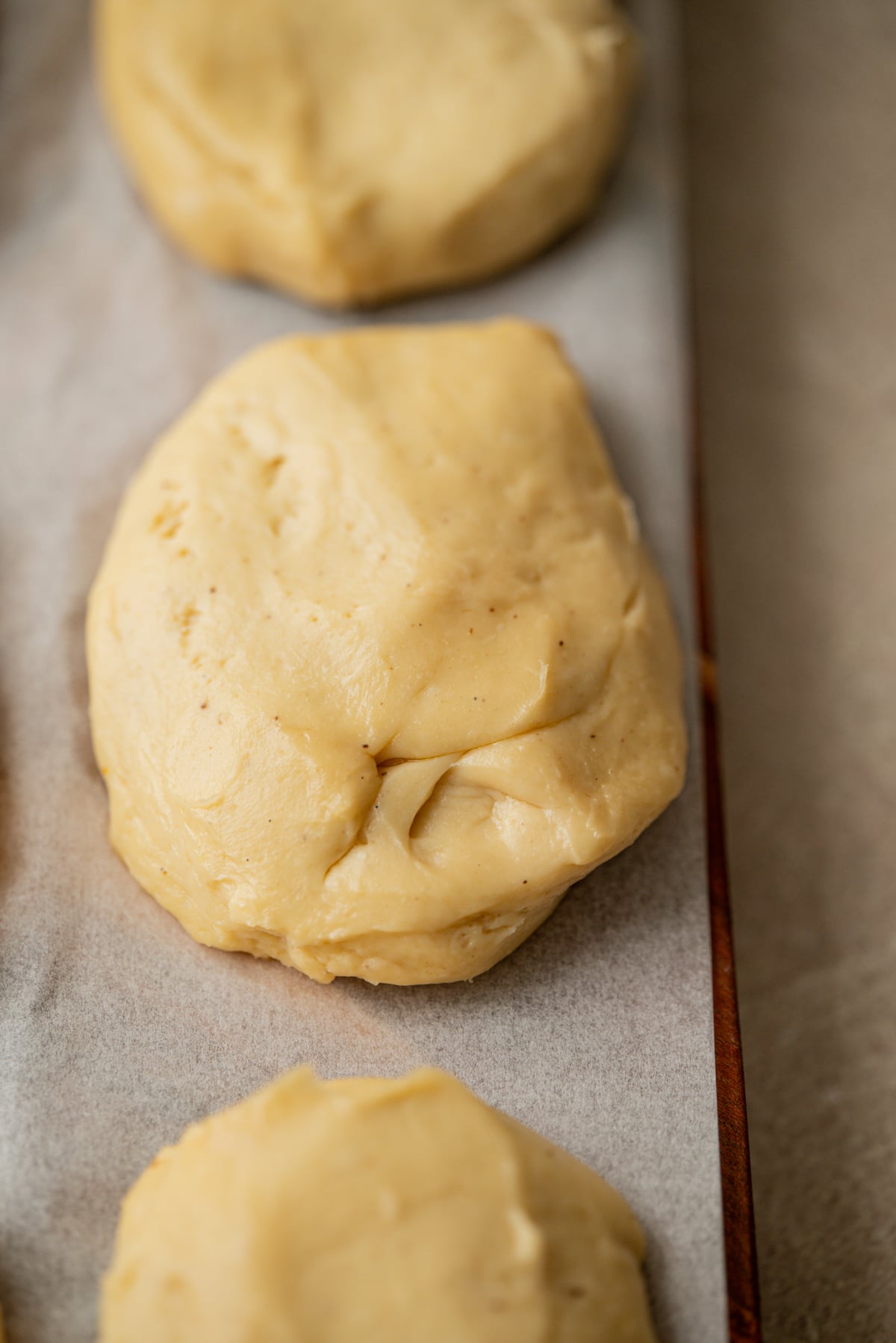 Three mounds of raw dough arranged on a parchment-lined baking sheet.