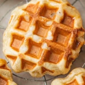 A round Belgian liege waffle with deep pockets, sitting on a wire cooling rack.
