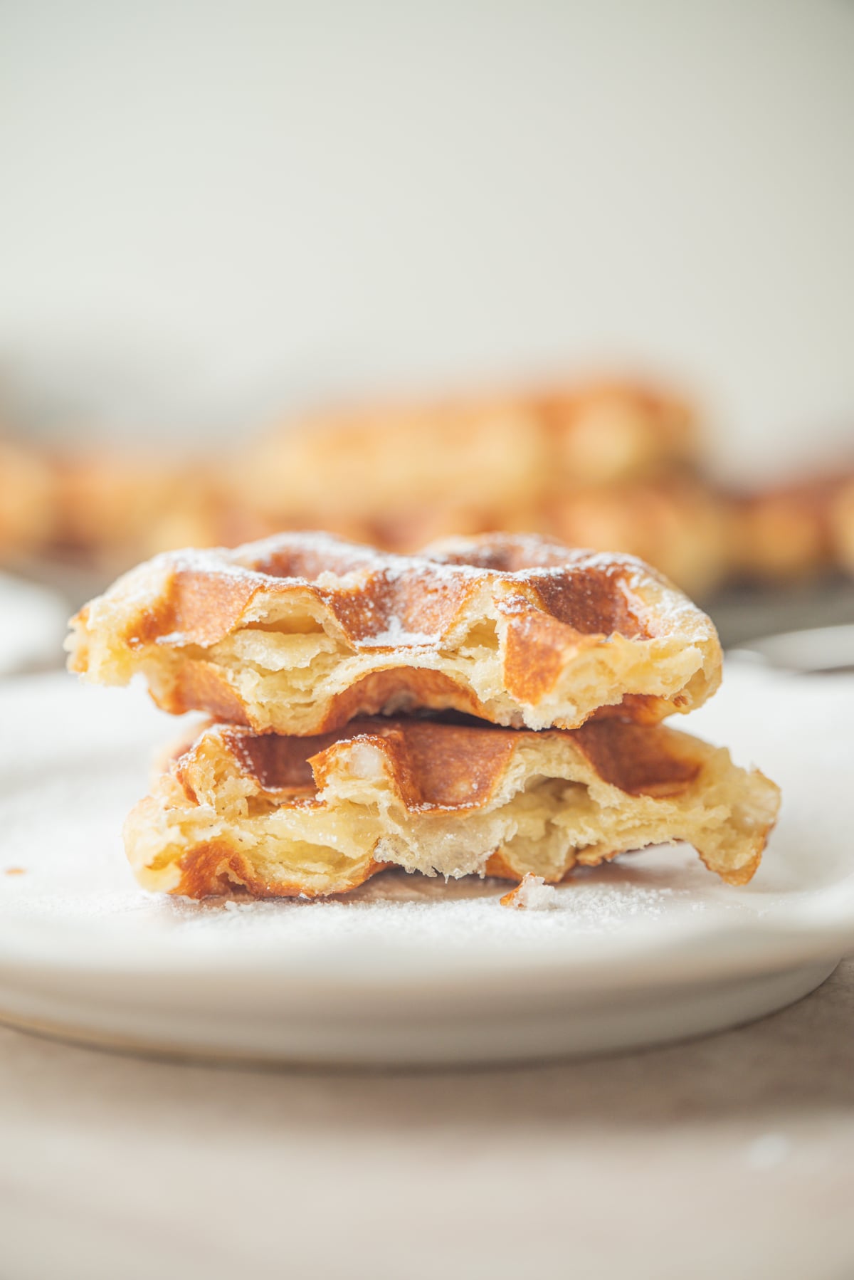 Two halves of a sourdough liege waffle sprinkled with powdered sugar, stacked on a white plate.