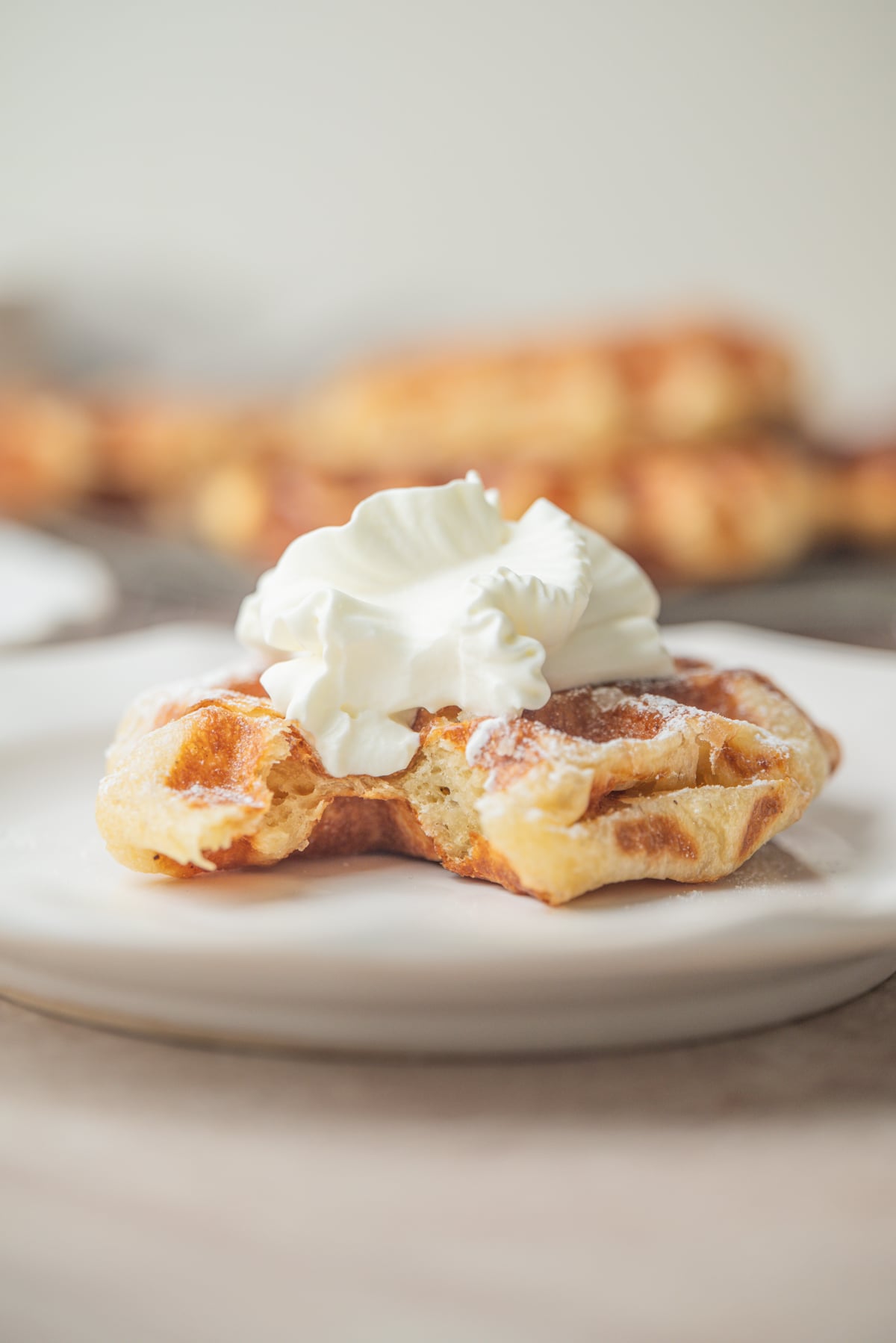 A single sourdough liege waffle topped with whipped cream on a white plate.
