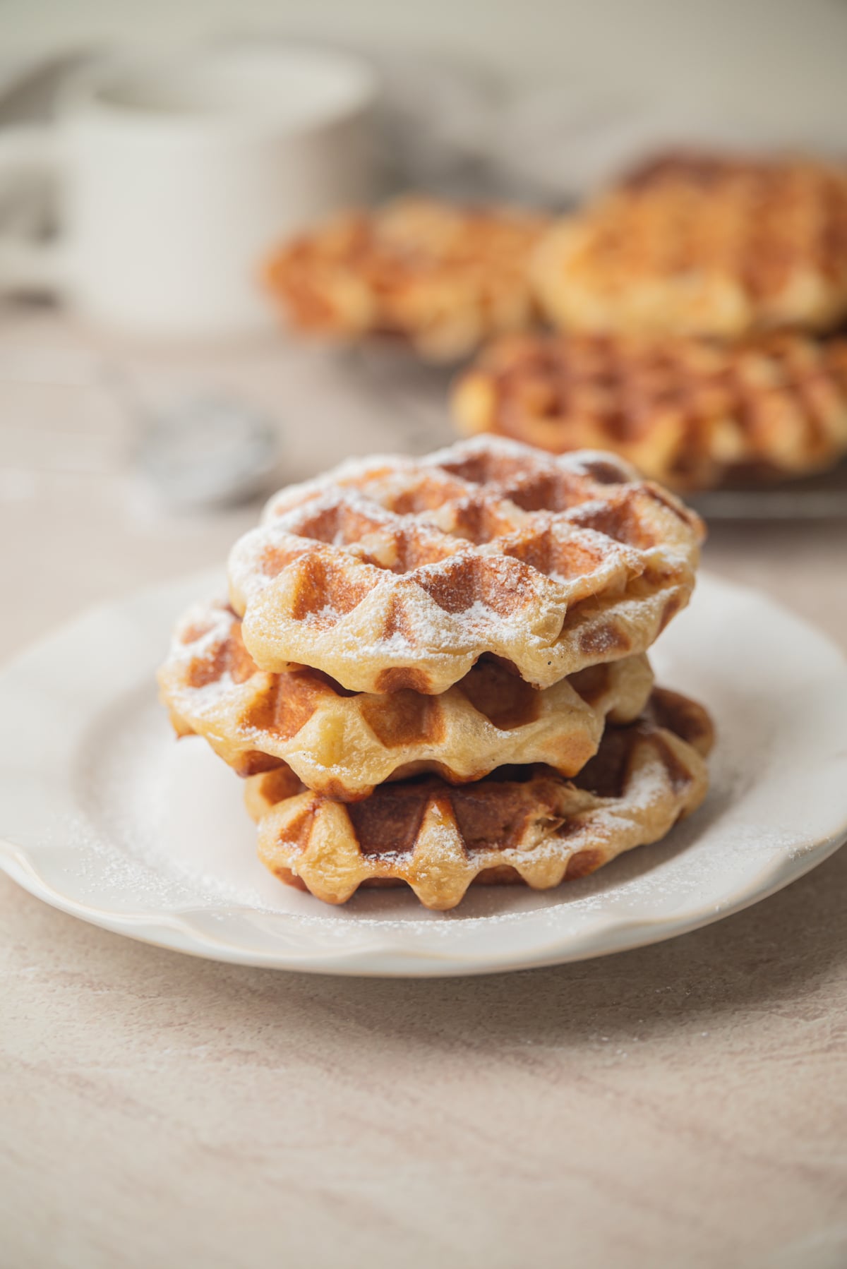 A stack of three golden-brown sourdough liege waffles dusted with powdered sugar on a white plate.