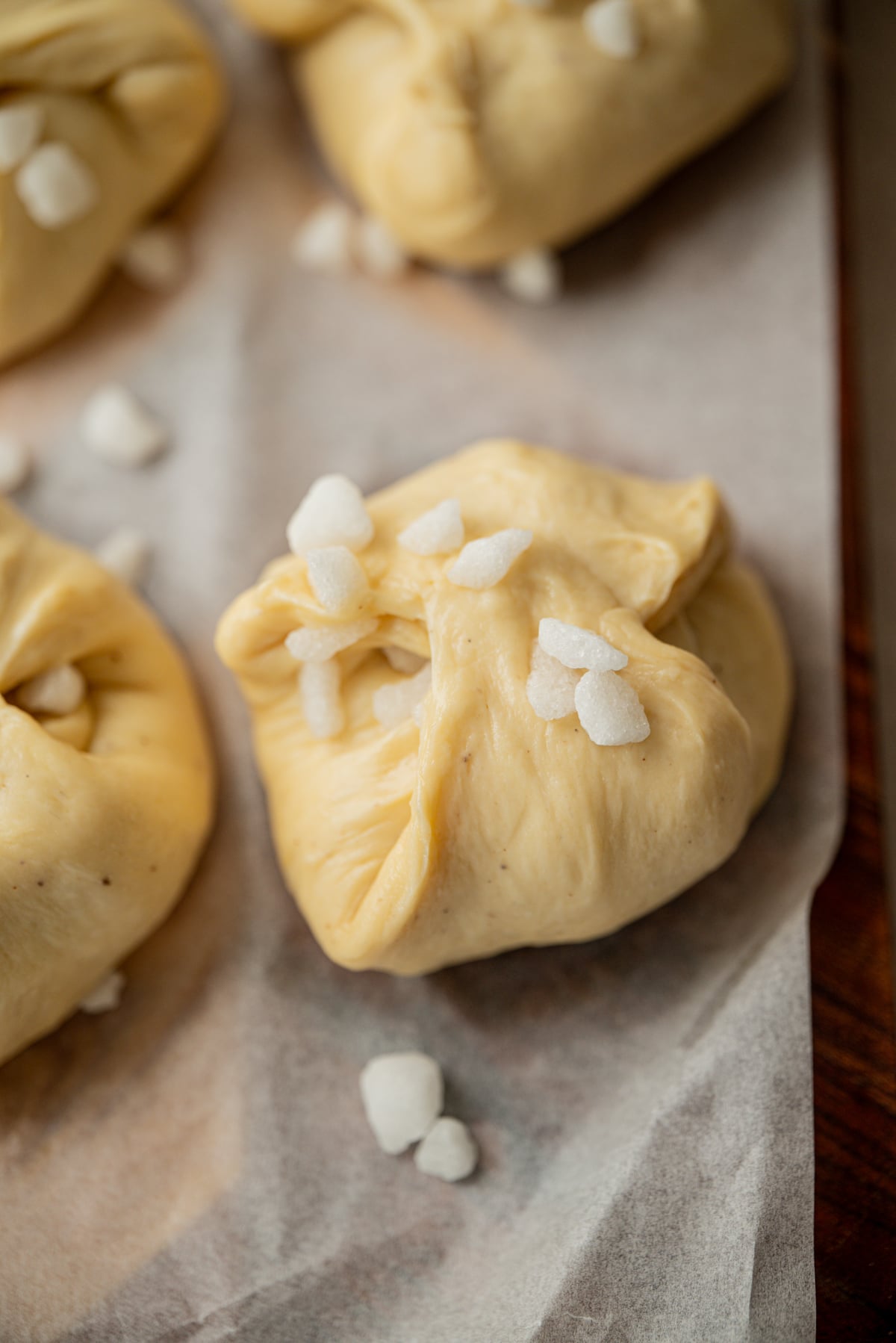 Unbaked buns topped with pearl sugar on parchment paper.